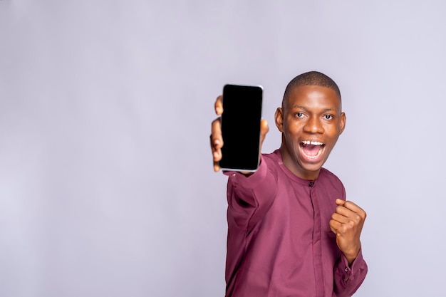 Smiling young african american man guy african clothing posing isolated on white wall background Hold mobile phone with blank empty screen People lifestyle concept