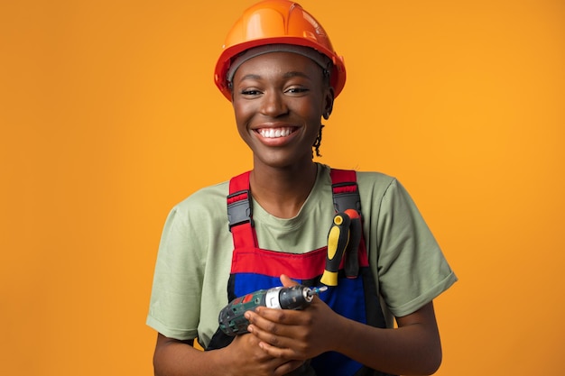 スタジオでドライバーツールを保持しているhardhatで若いアフリカ系アメリカ人女性の笑顔