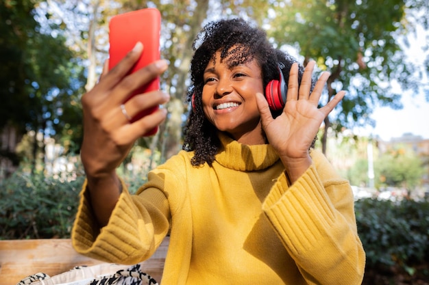 Sorridente giovane donna afroamericana onda mano sulla videochiamata utilizzando il telefono cellulare all'aperto. concetto di stile di vita e tecnologia.