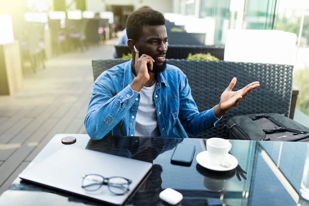 写真 コーヒーを飲みながら、カフェに座って携帯電話で話している若いアフリカ人の笑顔