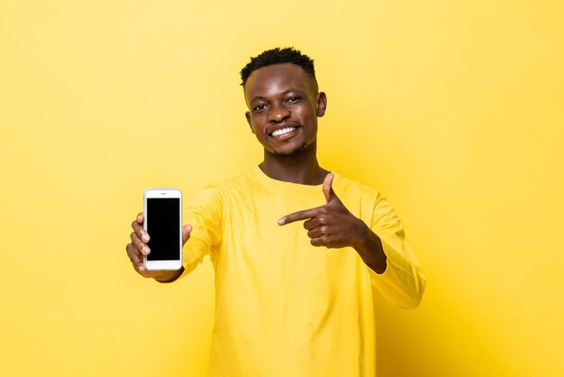 Sorridente giovane africano che punta la mano al telefono cellulare in giallo sfondo studio isolato