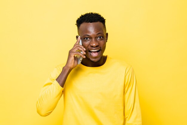 Smiling young African man talking on mobile phone in yellow isolated studio background