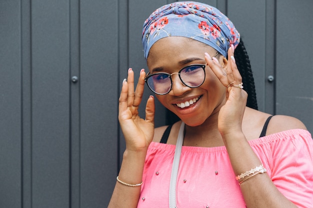 Smiling young african woman in a glasses posing against gray wall