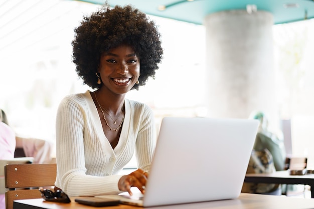 Smiling young african woman sitting with laptop in cafe