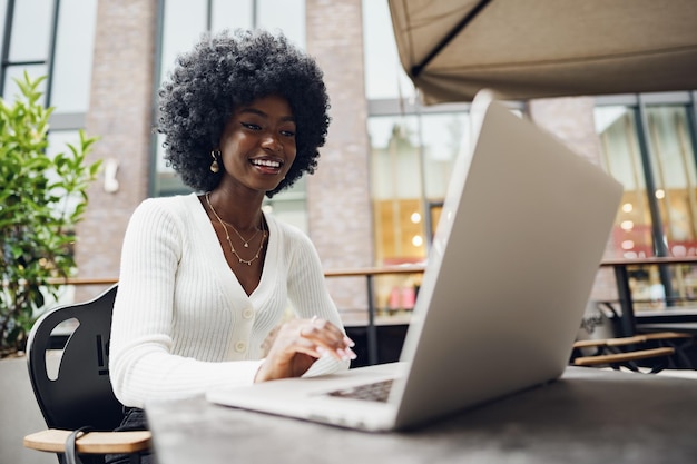 Smiling young african woman sitting with laptop in coffee shop