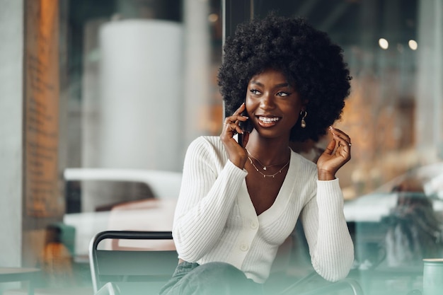 Smiling young african woman talking on cellphone at cafe