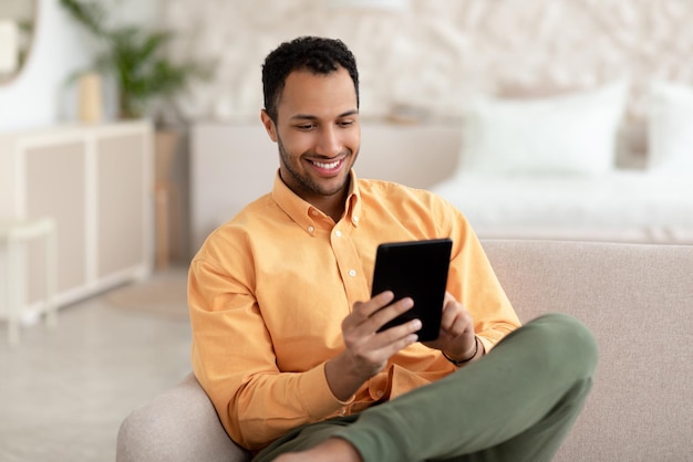 집에서 디지털 태블릿을 사용하여 웃고 있는 젊은 아랍 남자