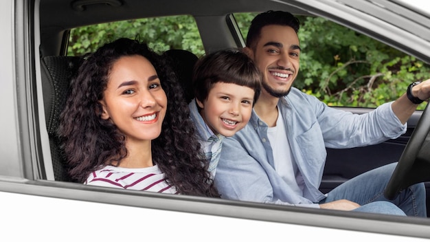 Photo smiling young arab man and woman with child are driving in car and looking at camera from open