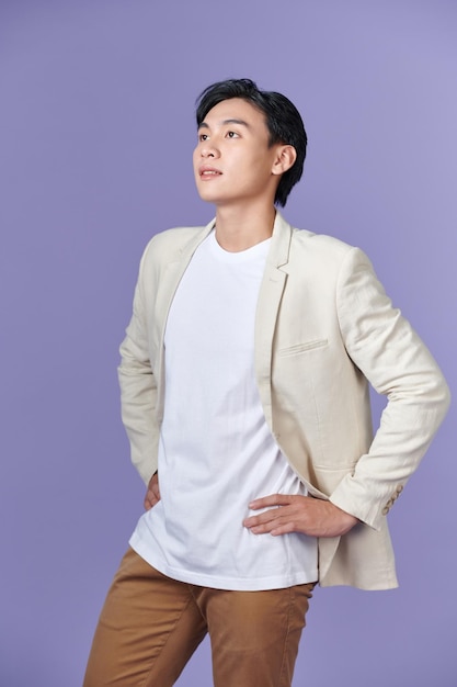 Smiling young Asian businessman in beige suit isolated on purple background