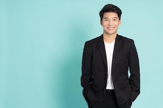 Smiling young Asian businessman in black suit isolated on green background