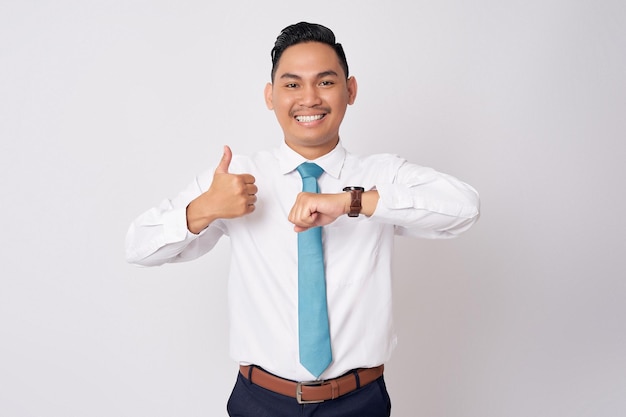 웃는 젊은 아시아 사업가 직원 회사 변호사 공식 셔츠 타이를 입고 시계와 엄지손가락을 보여주는  바탕에 고립되어 있습니다.