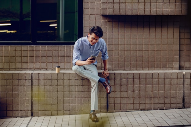 市内で携帯電話を使用して笑顔の若いアジア系のビジネスマン