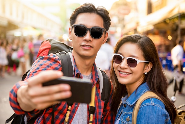 Giovani turisti asiatici sorridenti delle coppie che prendono selfie mentre viaggiando in strada bangkok tailandia di khao san durante le vacanze estive