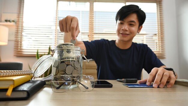 Smiling young asian male putting coin into the jar Save money for future retirement and financial planning concept