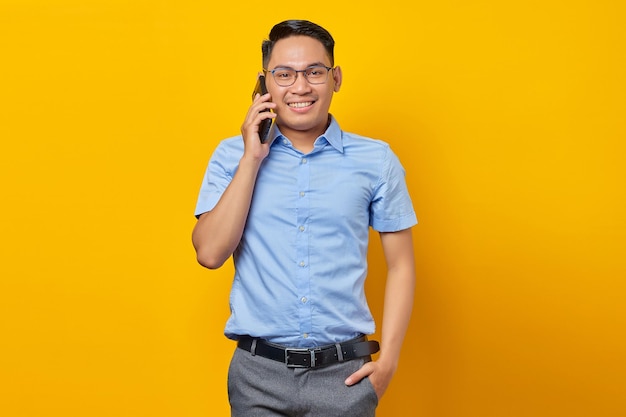 Smiling young asian man Asian in glasses talking on mobile phone isolated on yellow background businessman and entrepreneur concept