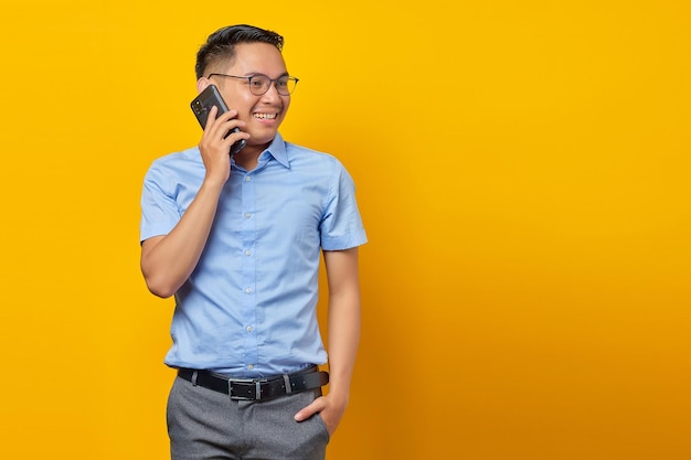 Smiling young asian man asian in glasses talking on mobile phone isolated on yellow background businessman and entrepreneur concept