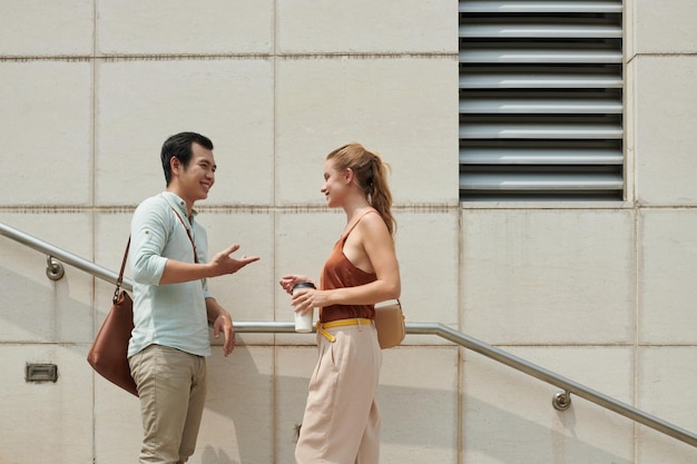 Photo smiling young asian man asking out young woman when that are standing on steps outdoors