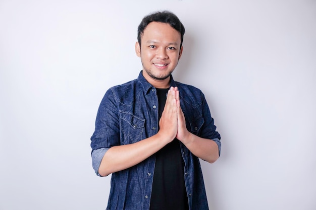 Smiling young Asian man gesturing traditional greeting isolated over white background