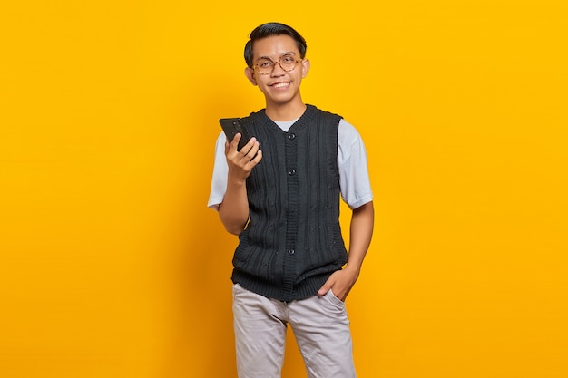 웃고 있는 젊은 아시아 남성이 휴대전화로 통화하고 노란색 배경에서 카메라를 바라보고 있다