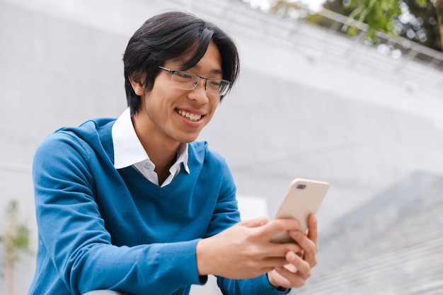 写真 屋外の階段に座って携帯電話で話している若いアジア人男性の笑顔