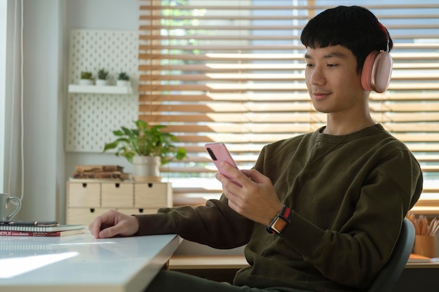 Smiling young asian man wearing wireless headphone using mobile phone