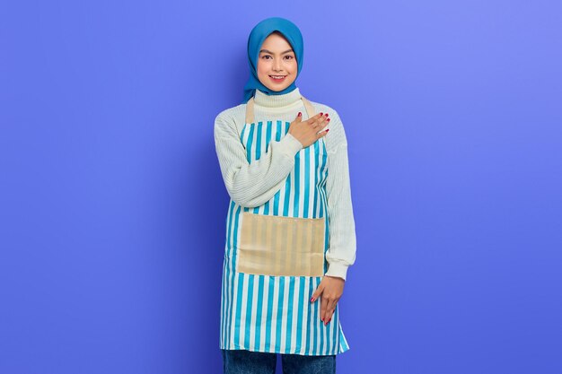 Smiling young Asian Muslim woman in 20s wearing hijab and apron open sign to greet and greet customers isolated on purple background People housewife muslim lifestyle concept