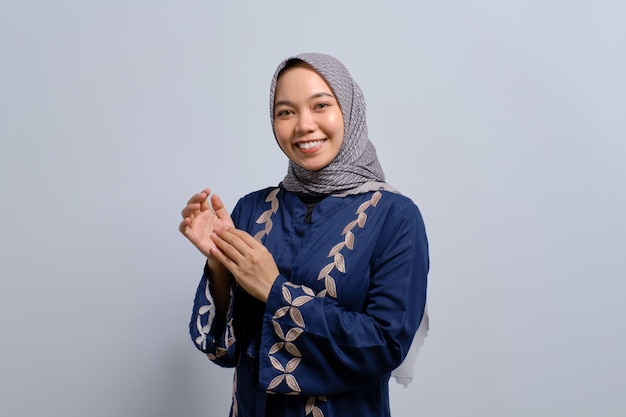 흰색 배경 위에 격리된 행복한 표정으로 성공을 축하하며 손뼉을 치며 웃고 있는 젊은 아시아 무슬림 여성