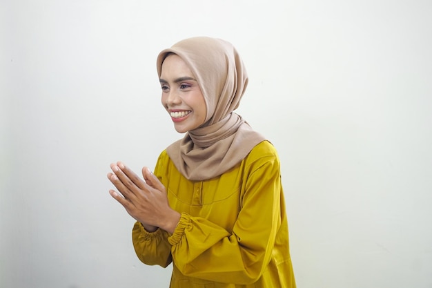 Smiling young Asian Muslim woman gesturing Eid Mubarak greeting isolated over white background