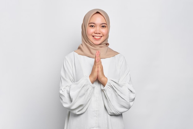 Smiling young Asian Muslim woman gesturing Eid Mubarak greeting isolated over white background