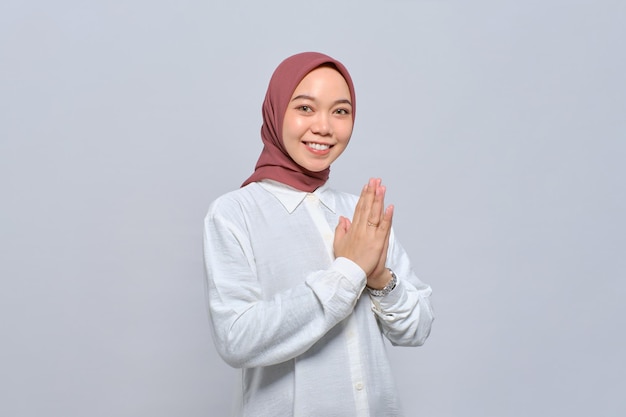 Smiling young Asian Muslim woman gesturing Eid Mubarak greeting isolated over white background