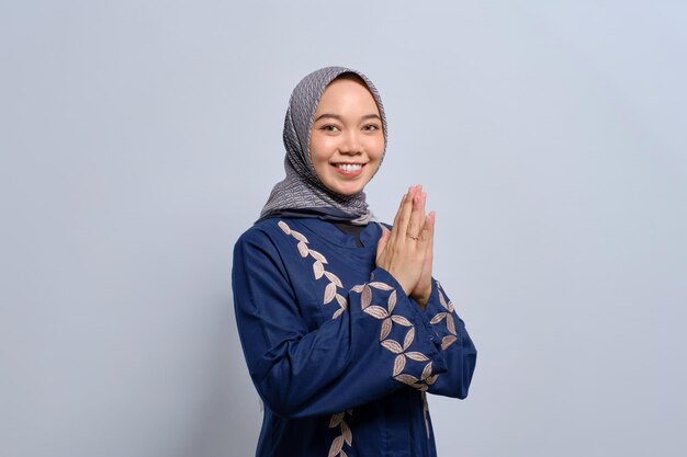 Smiling young Asian Muslim woman gesturing Eid Mubarak greeting isolated over white background