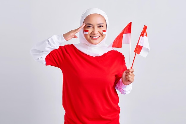 Smiling young Asian muslim woman in red white tshirt holding flag indonesian to celebrating indonesian independence day on 17 august and showing respect gesture isolated on white background