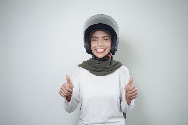 오토바이 헬멧을 사용하여 두 엄지손가락을 보여주는 웃는 젊은 아시아 이슬람 여성