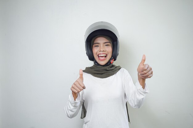 Smiling young Asian muslim woman showing thumbs up using motorcycle helmet