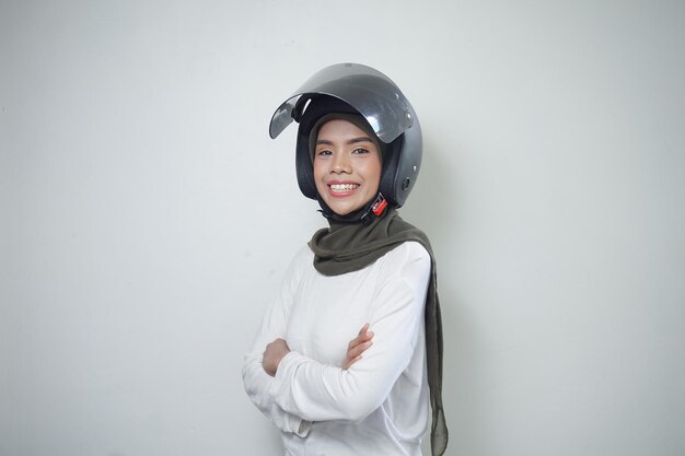 白い背景で隔離のオートバイのヘルメットを使用して笑顔の若いアジアのイスラム教徒の女性