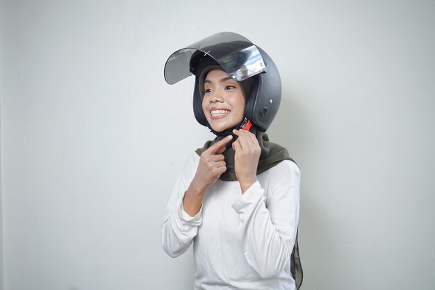 白い背景で隔離のオートバイのヘルメットを使用して笑顔の若いアジアのイスラム教徒の女性