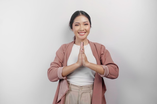 Photo a smiling young asian woman employee wearing a cardigan gestures a traditional greeting isolated over white background