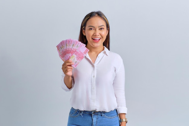 白い背景に分離されたお金の紙幣を保持している笑顔の若いアジア女性
