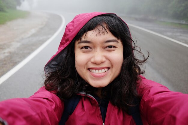 笑顔の若いアジア人女性が熱帯雨林で旅してセルフィーを撮り 霧で雨を降らせています