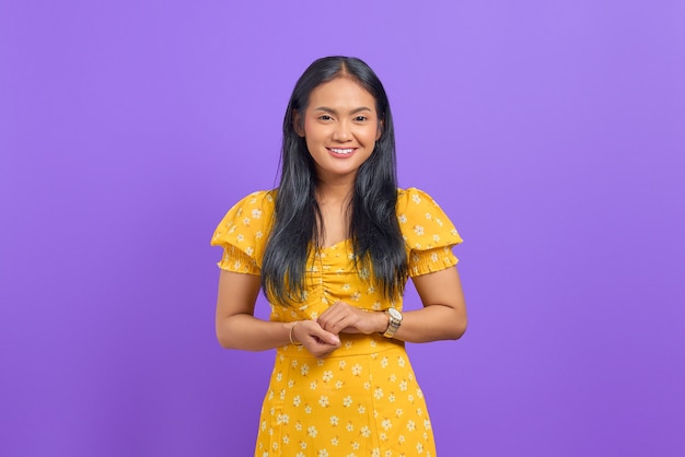 Smiling young asian woman keeps hand together and feels optimistic on purple background