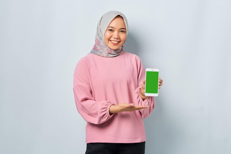 Smiling young Asian woman in pink shirt showing mobile phone blank screen recommending App isolated over white background