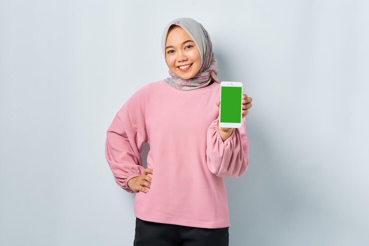 Smiling young Asian woman in pink shirt showing mobile phone blank screen recommending App isolated over white background