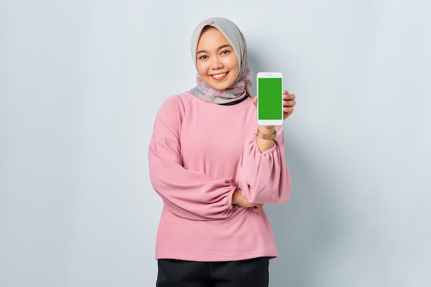 Smiling young asian woman in pink shirt showing mobile phone
blank screen recommending app isolated over white background