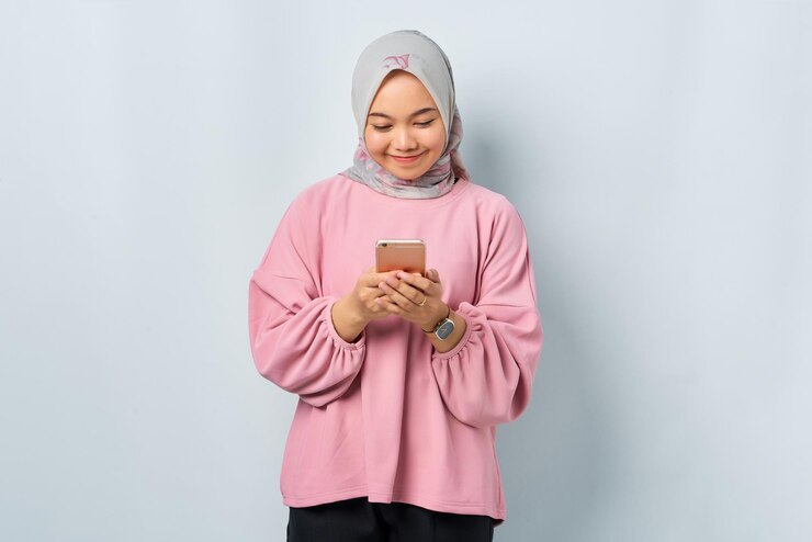 Smiling young Asian woman in pink shirt using mobile phone and received good news isolated over white background