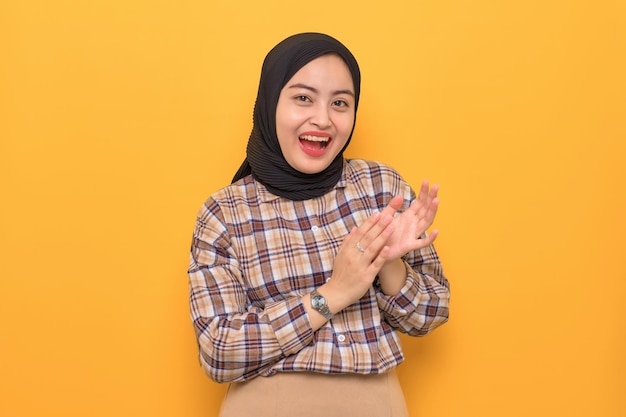 Smiling young Asian woman in plaid shirt clapping hands celebrating success congratulating someone isolated on yellow background