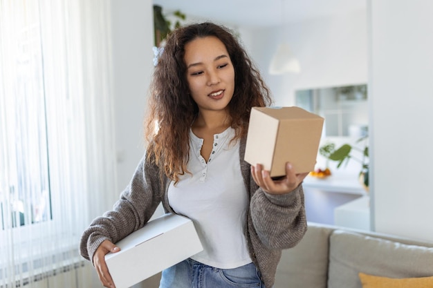 Smiling young Asian woman shopping online with smartphone on hand receiving a delivered parcel by home delivery service Online shopping online banking Enjoyable customer shopping experience