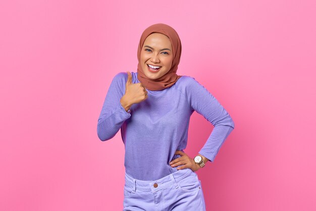 Smiling young Asian woman showing approval with thumb up gesture on pink background