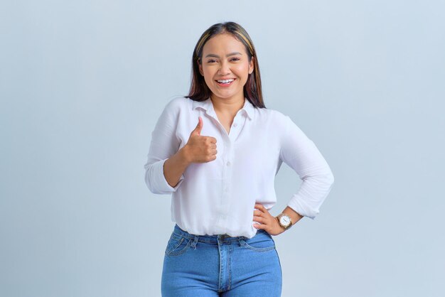 Smiling young Asian woman showing thumb up gesture recommending something good isolated over white background