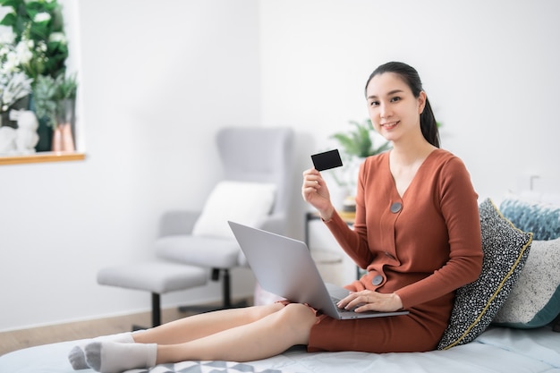 Smiling young Asian woman using a credit card in her home