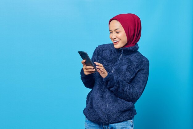 파란색 배경에 스마트폰을 사용하여 웃고 있는 젊은 아시아 여성